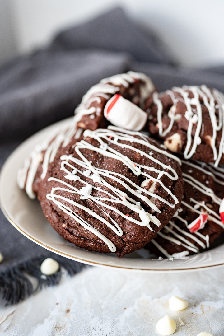 chocolate cookies with peppermint and white chocolate chips in side with a white chocolate drizzle. The cookies are in a bowl on the counter.