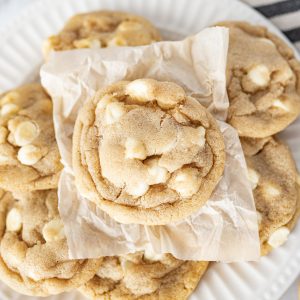 A pile of white chocolate chip cookies on a white plate.