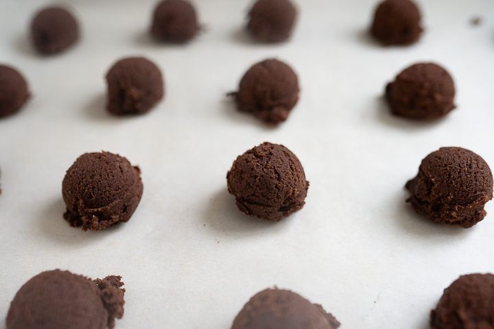 Balls of chocolate cookie dough arranged on parchment paper ready to bake.