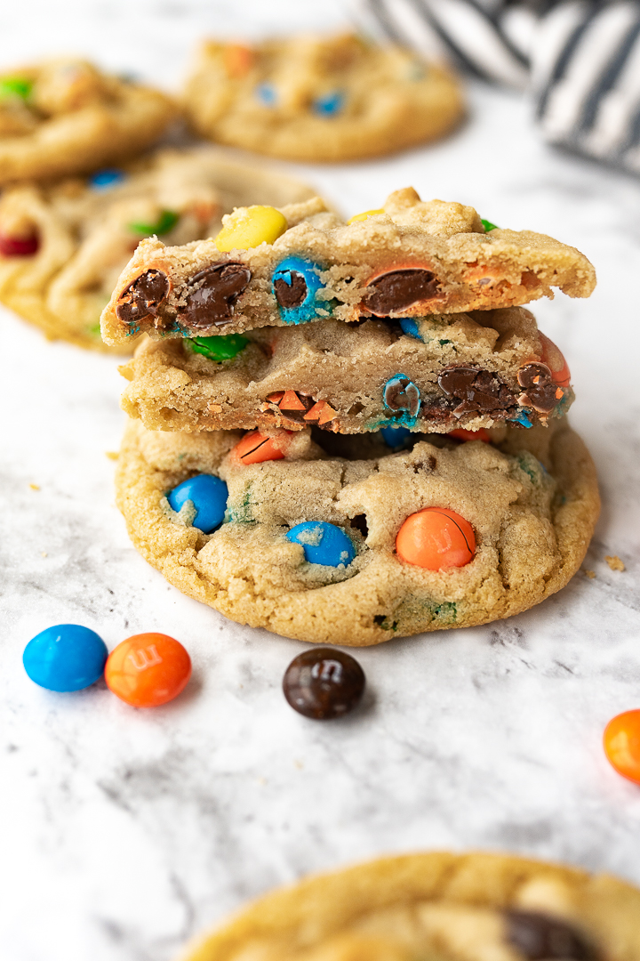 M&M cookies on the counter with a few cut in half so you can see the colorful M&Ms inside the cookies.
