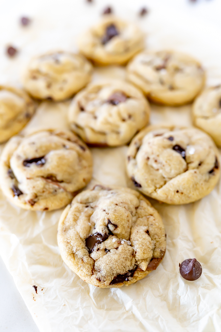 Chocolate chip cookies on parchment paper with chocolate chips sprinkled around them.