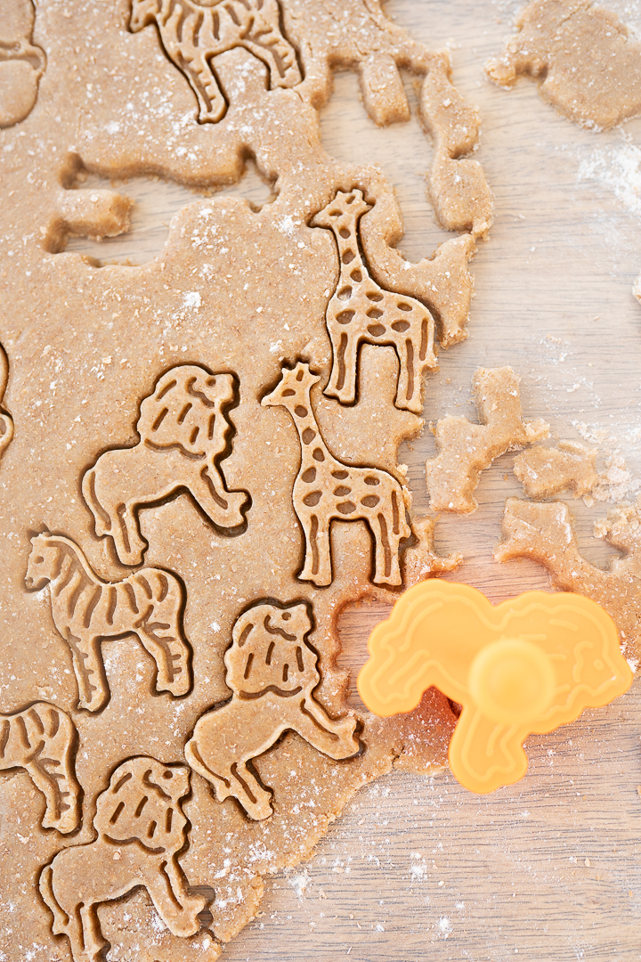 Animal cookie dough rolled out on the counter with a few animal shapes cut out of the dough.