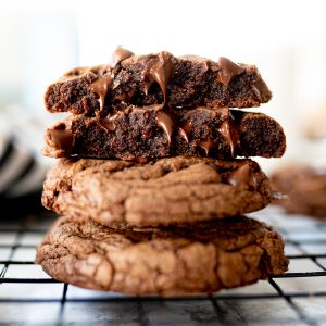 Chocolate Chip cookies made from brownie mix stacked on top of each other on a cooling rack with melty chocolate chips oozing out.