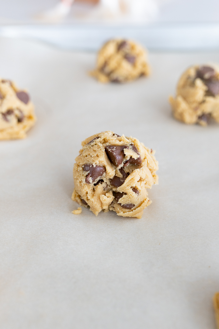 Balls of chocolate chip cookie dough on parchment paper on the counter.
