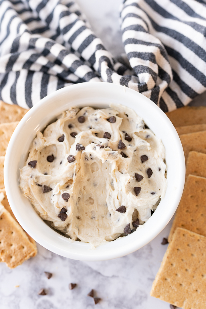A bowl of dip on the counter with a scoop taken out of the bowl and crackers and chocolate chips in the background.
