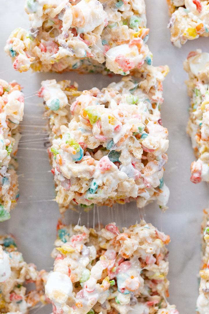 Fruity pebbles treats being pulled apart on the counter so you can see the melted marshmallow strings.