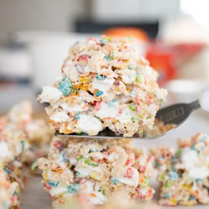 A fruity pebbles treat on a spatula with marshmallows oozing out.