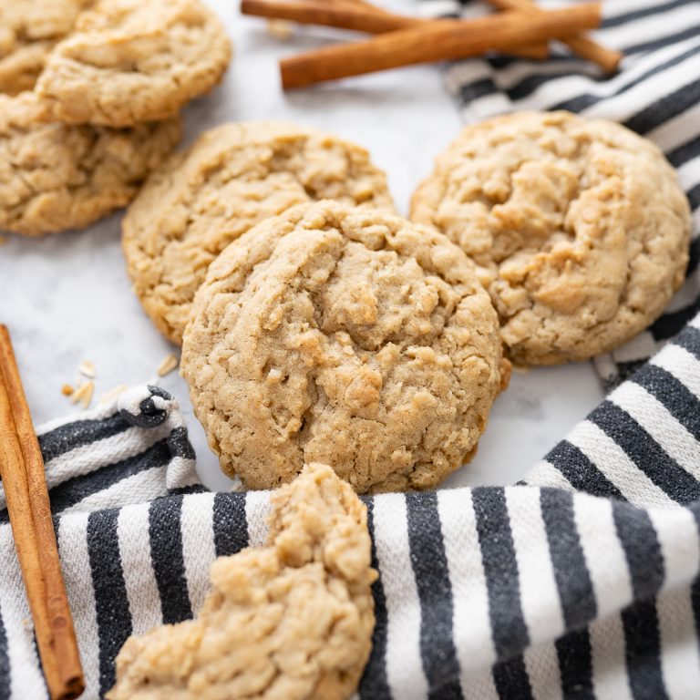 Oatmeal cookies and cinnamon sticks on the counter with a striped dish towel in the background.