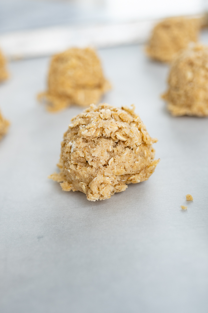 Balls of oatmeal cookie dough on parchment paper before baking.