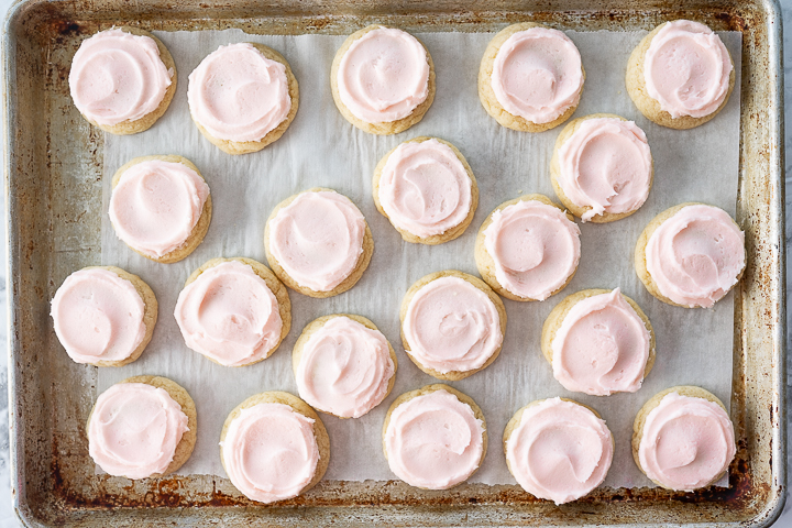 A cookie sheet filled with small, pink frosted, crumbl copycat sugar cookies.