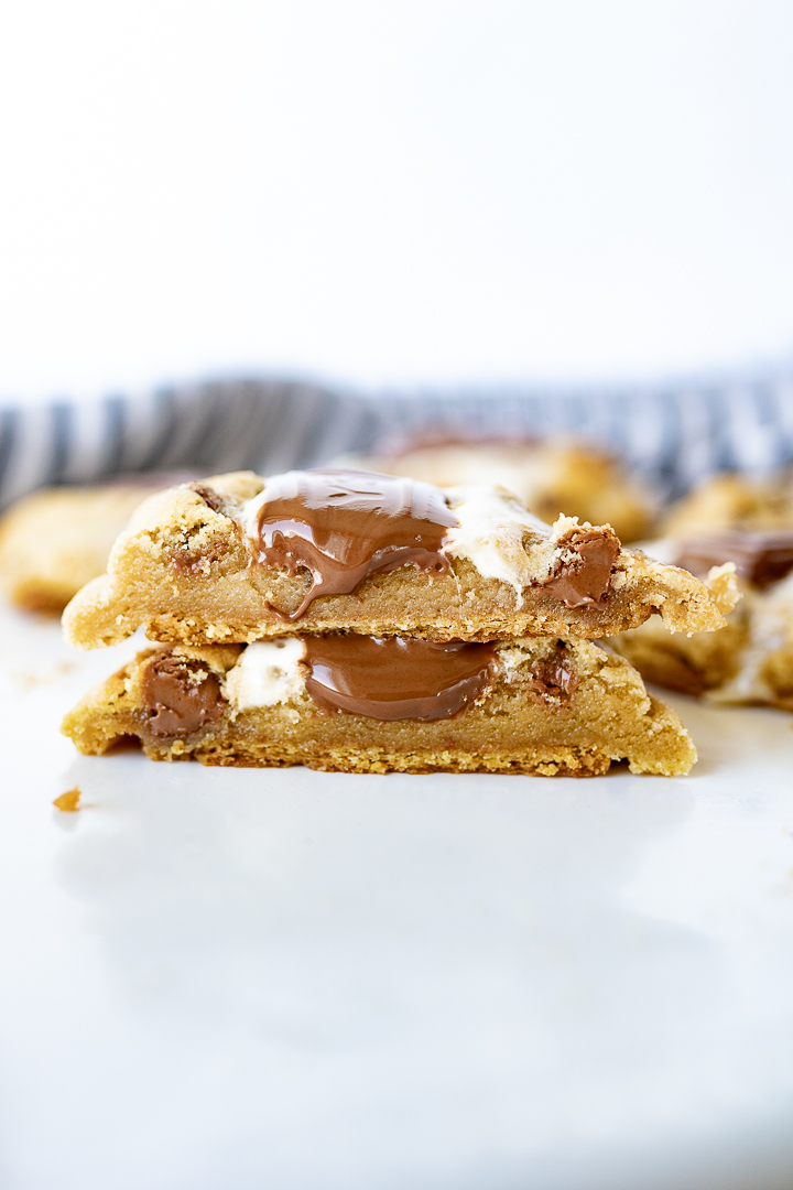 Smores cookies cut in half and stacked on top of each other with melted chocolate and marshmallows melting out of the cookies.