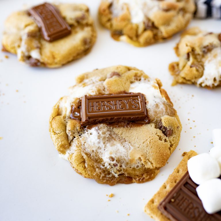 Several smores cookies on the counter with a piece of hershey's chocolate on top of each cookie.