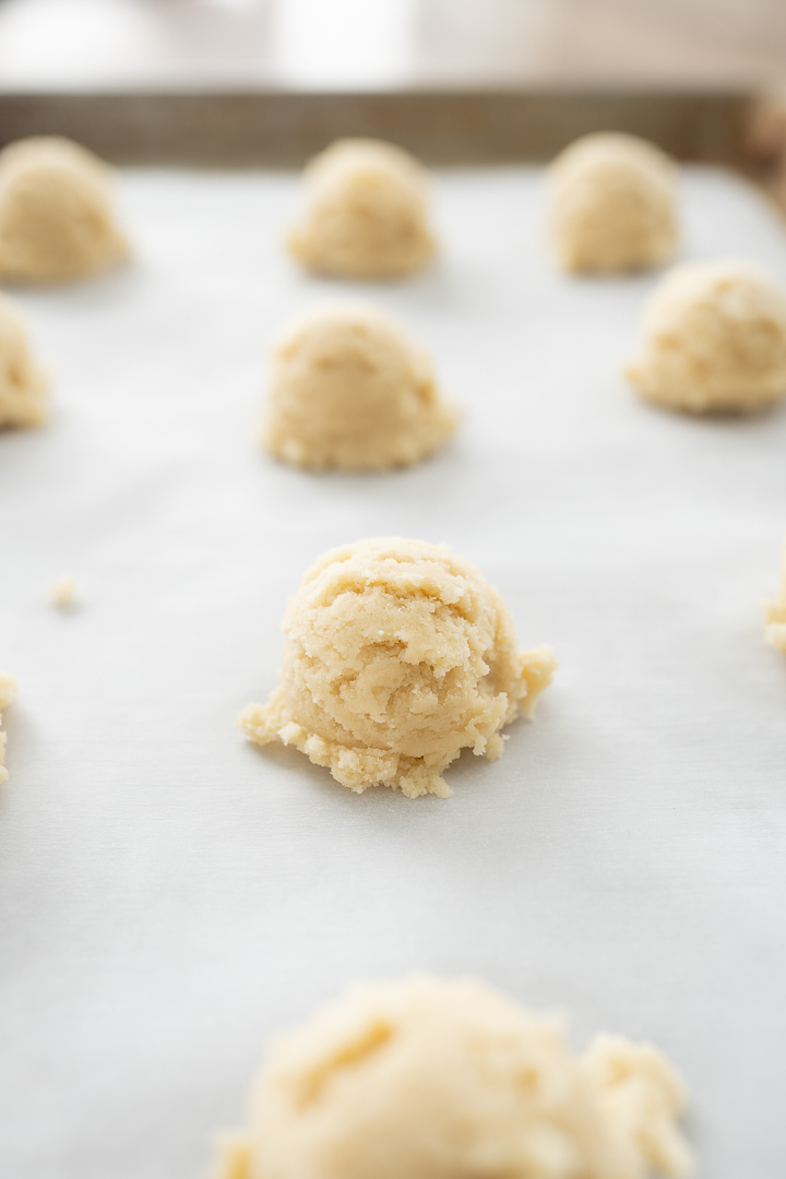 Balls of sugar cookie dough on a cookie sheet before baking.