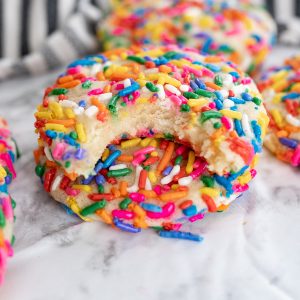 Rainbow sprinkle cookies stacked on top of each other with a bite taken out of the top cookie.