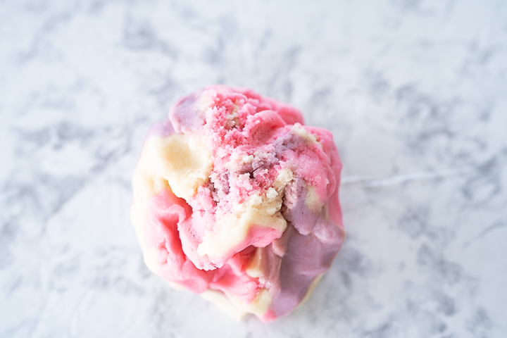 A ball of cookie dough with pink, purple, and regular dough tie dyed together.