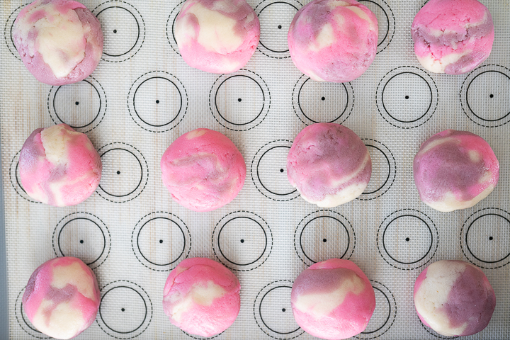 Pink and purple balls of tie dye cookie dough on a baking sheet.