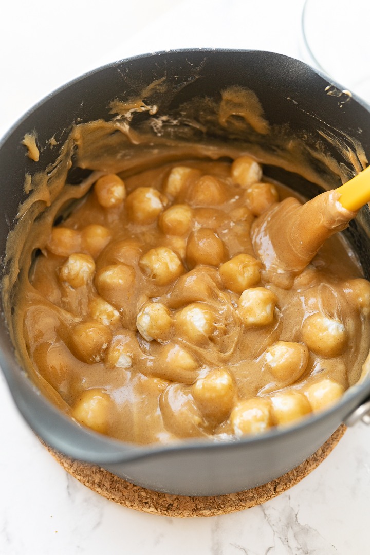 A pot with mini marshmallows coated in a saucy peanut butter mixture on the counter.