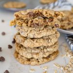 Great harvest copycat oatmeal cookies stacked on the counter with chocolate chips and oatmeal sprinkled around them.