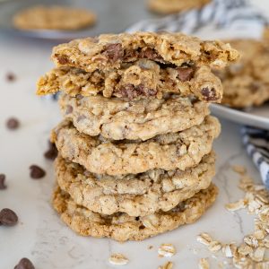 Great harvest copycat oatmeal cookies stacked on the counter with chocolate chips and oatmeal sprinkled around them.