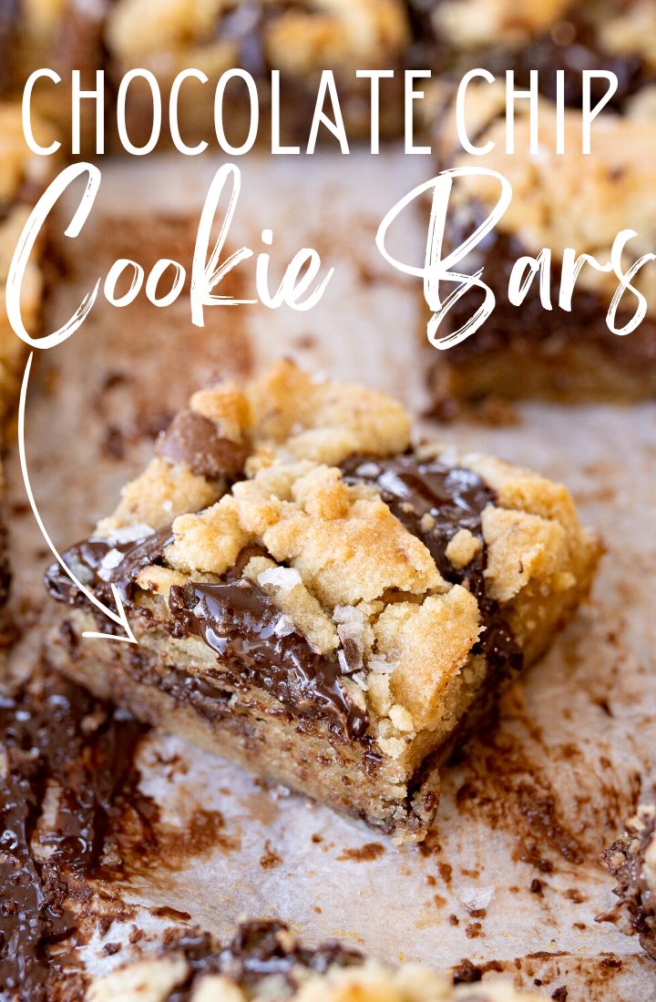 A cookie bar on the counter with chocolate in the background and text on the photo that reads "chocolate chip cookie bars."