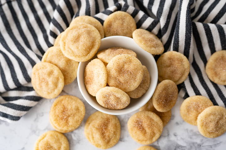 A small white bowl filled with mini snickerdoodles and other tiny cookies surrounding the bowl on the counter.