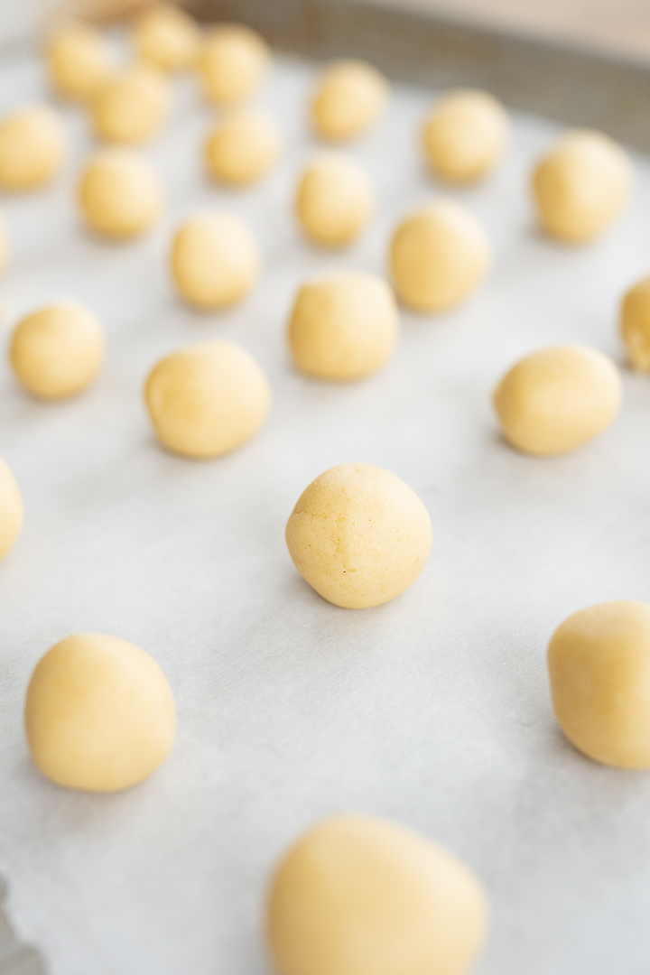 Small balls of sugar cookie dough on parchment paper before baking.