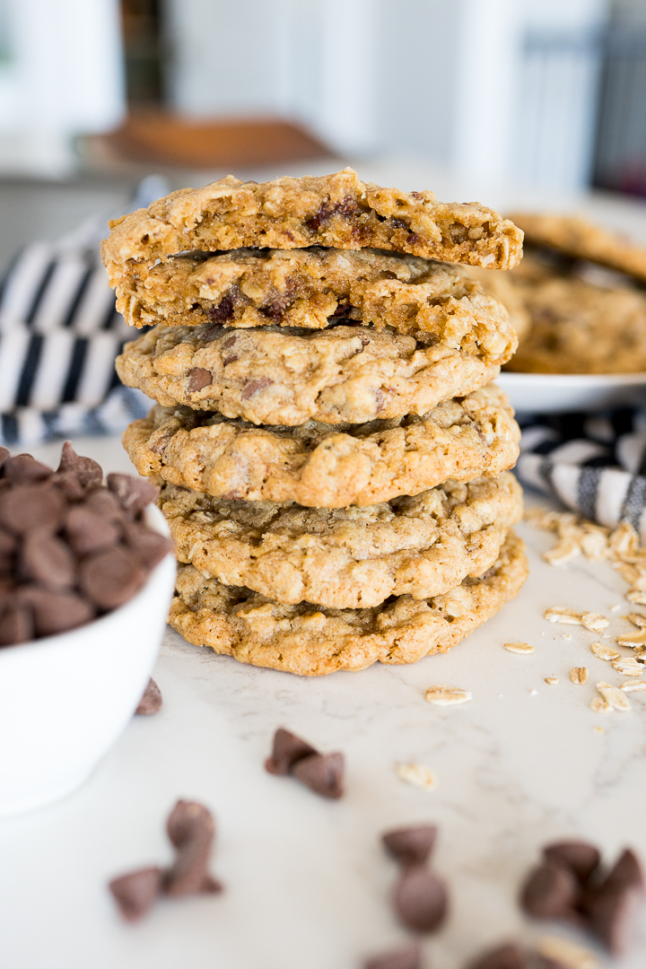 Great harvest oatmeal cookies stacked on the counter with a bowl of chocolate chips.