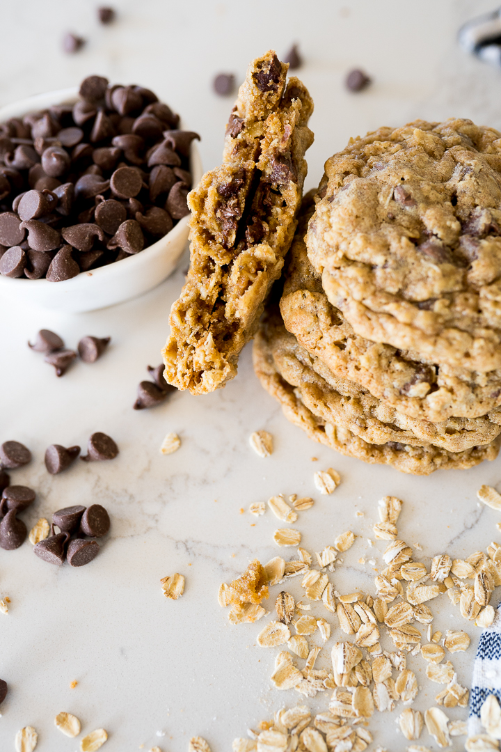 Great harvest copycat oatmeal cookies on the counter with chocolate chips and oatmeal sprinkled around them.