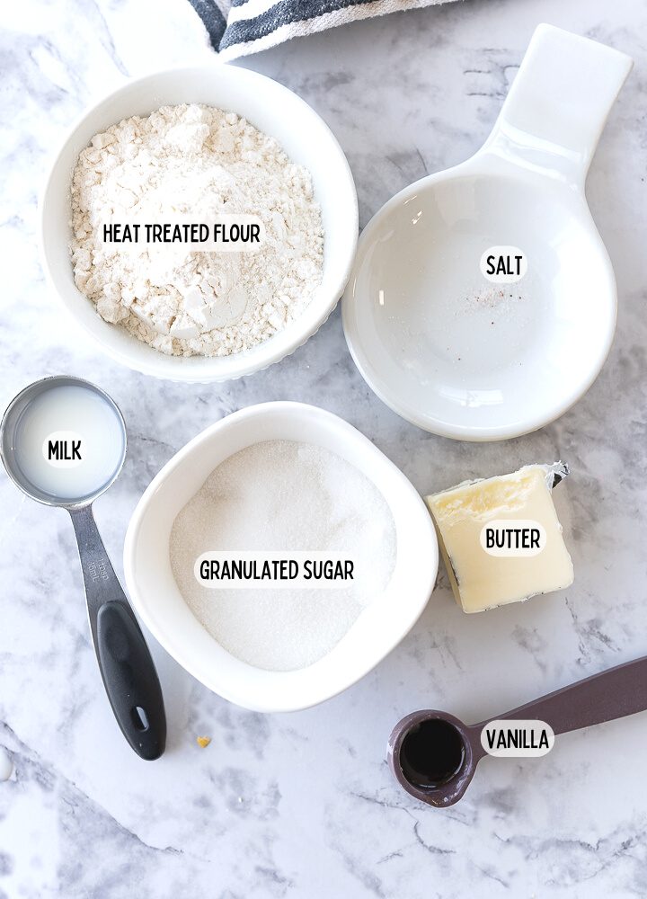 Ingredients for edible sugar cookie dough on the counter including: heat treated flour, milk, vanilla, butter, sugar, and salt.