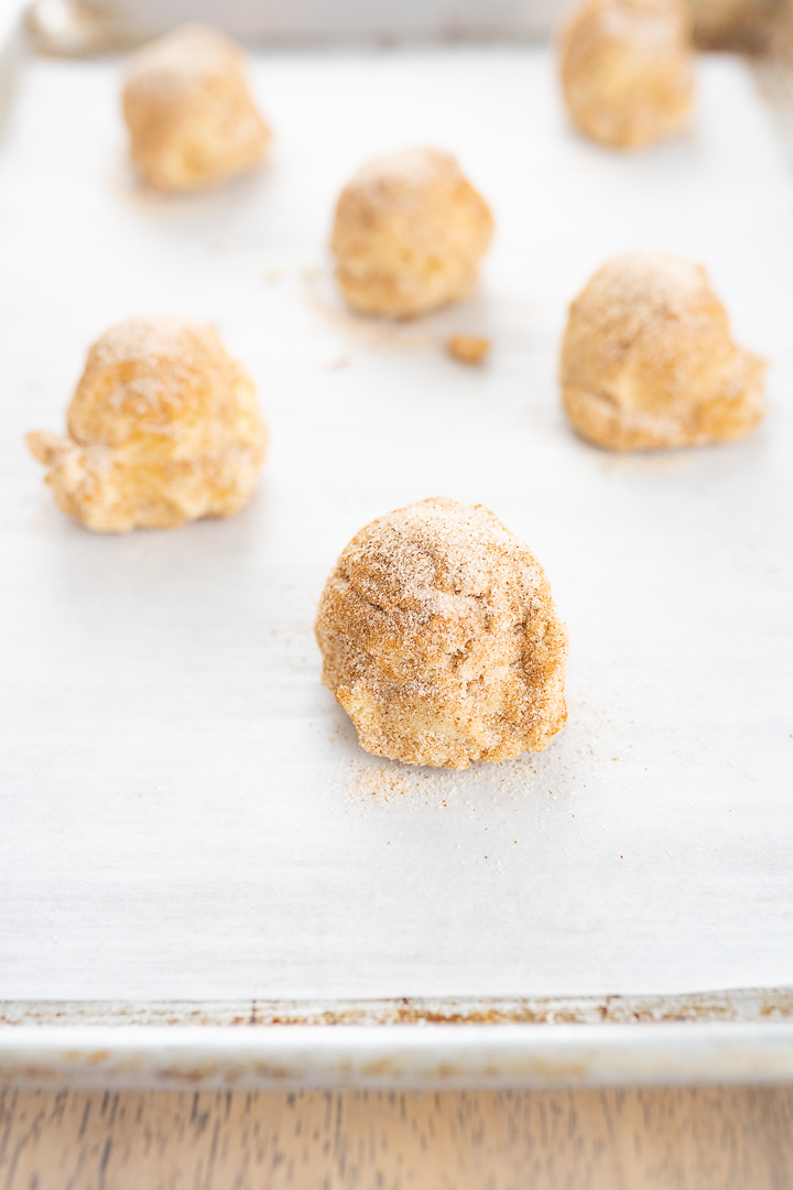 Balls of cookie dough that have been rolled in cinnamon sugar on a baking sheet.