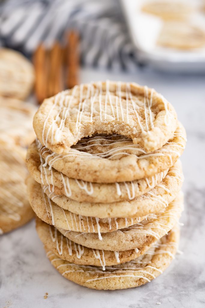A stack of cinnamon roll cookies on the counter with cinnamon sticks in the background.