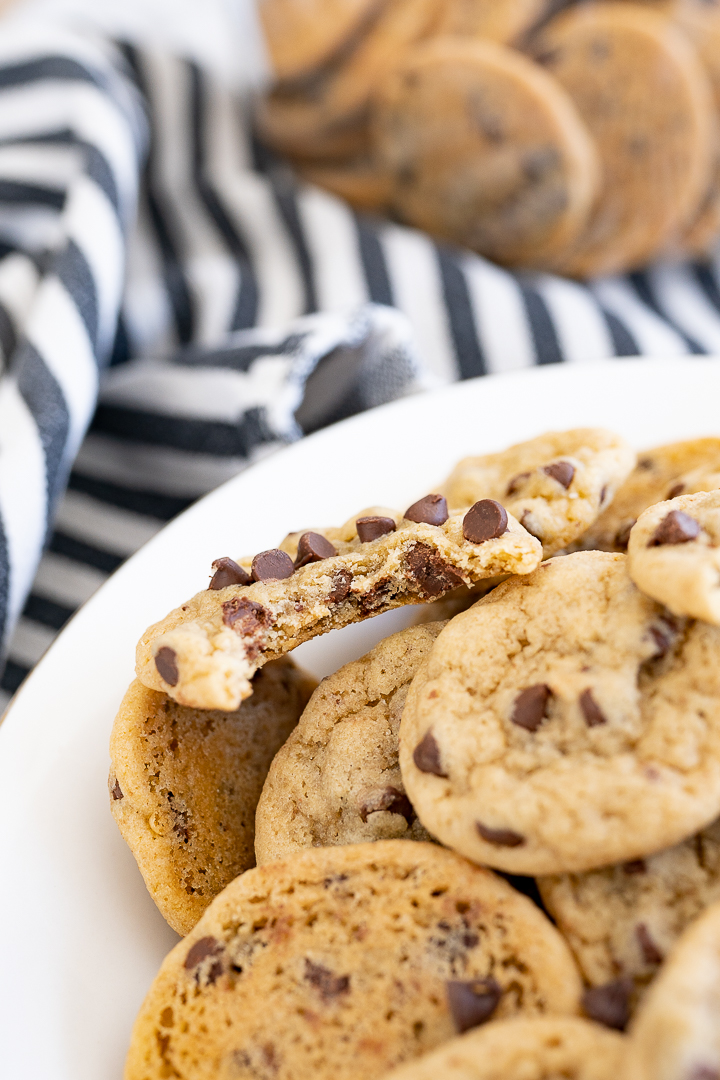 Up close of a bowl of mini chocolate chip cookies with one cookie missing a bite and a striped towel in the background.