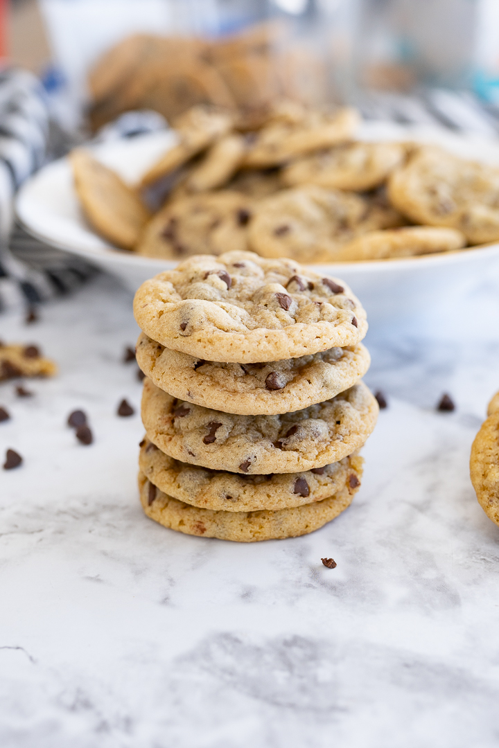 A stack of costco mini cookies on the counter with chocolate chips sprinkled and more cookies in the background.