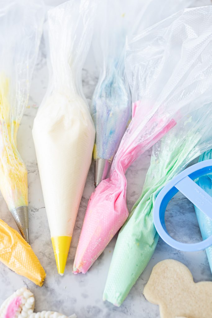 Several piping bags full of different pastel colored frosting on the counter.