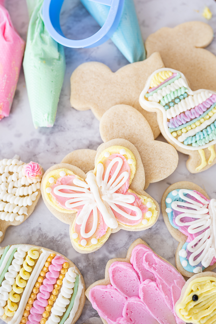 Several easter sugar cookies on the counter and frosted in pastel pink, yellow, and white.