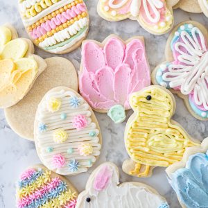 Frosted Easter sugar cookies on the counter including a chick, flower, egg, and butterfly cookie. All shape cookies without a cookie cutter.
