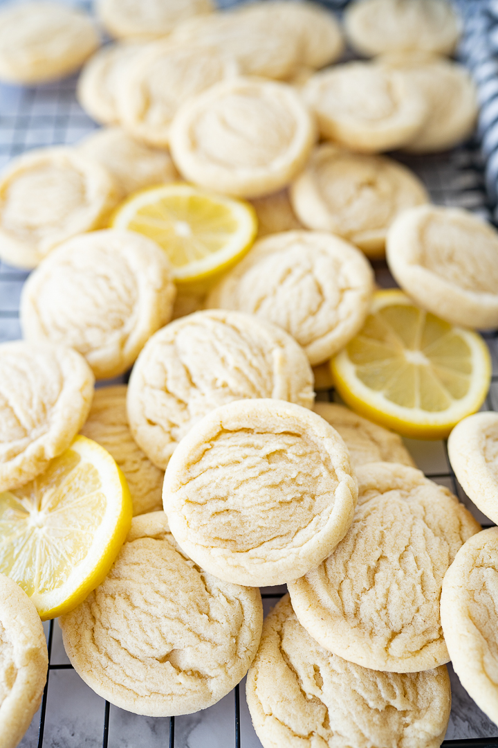 Several lemon sugar cookies and slices of lemon on a cooling rack on the counter.