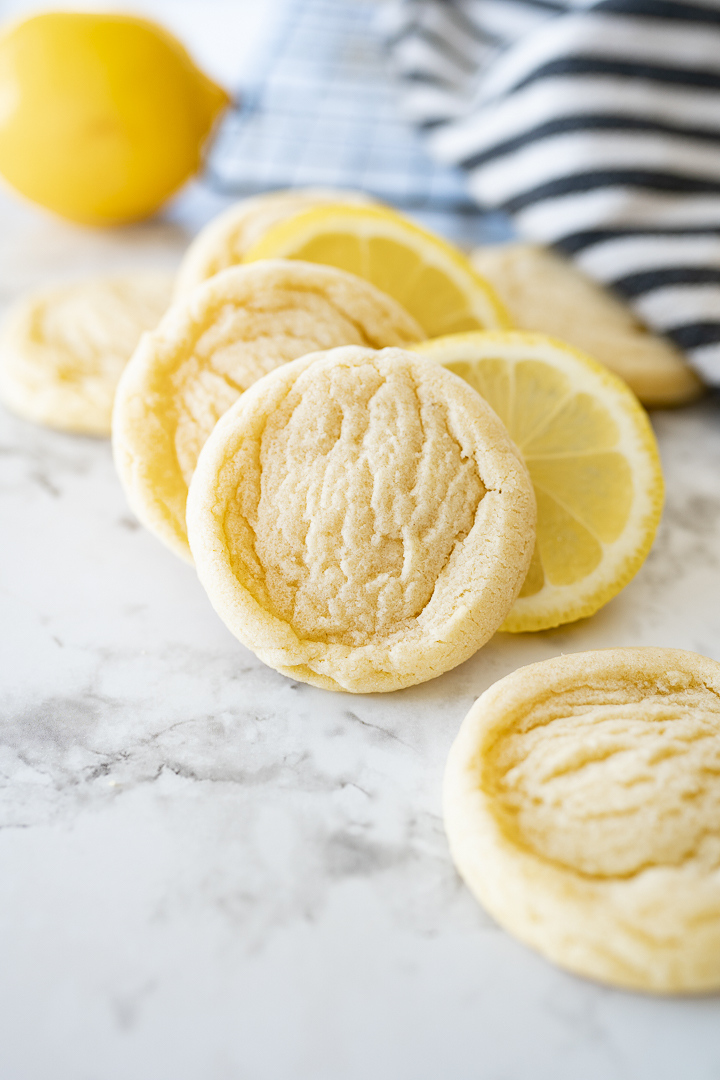 Lemon cookies, lemon slices, and full lemons on the counter with a striped towel in the background.