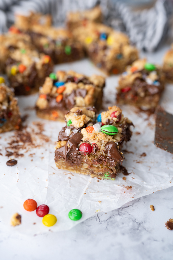 Side view of chocolatey cookie bars on parchment paper with M&Ms sprinkled on the counter.