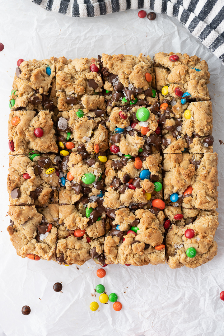 Baked cookie bars with M&Ms that are laying on parchment paper and cut into squares.