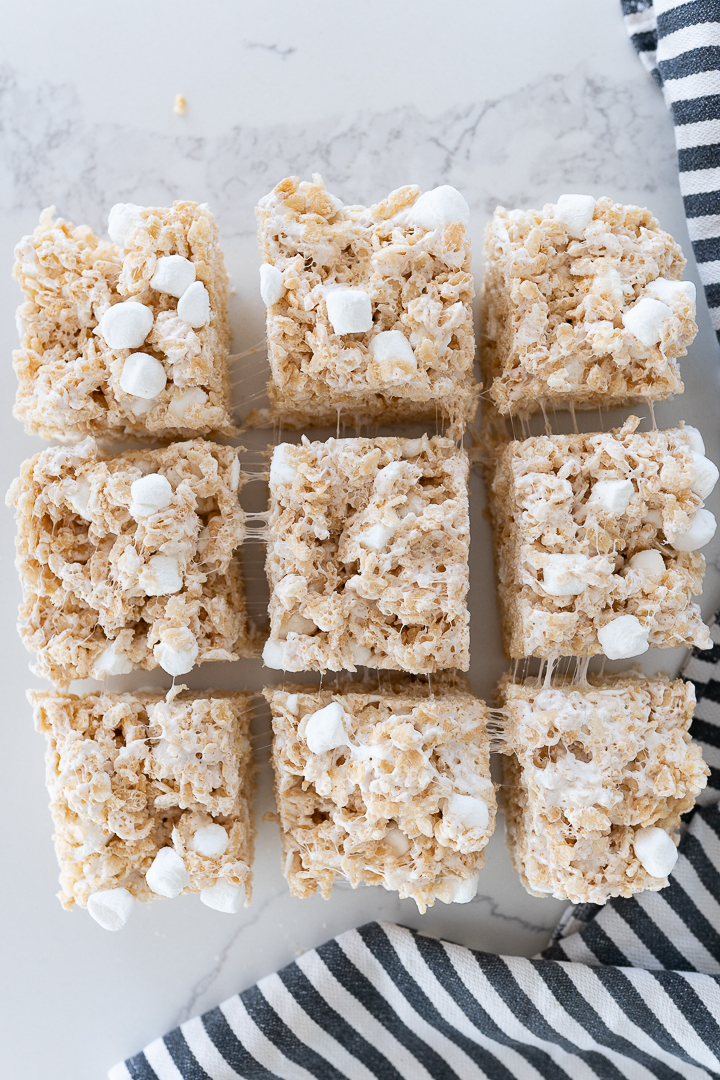 A grid of 9 square rice krispy treats on a counter with a black and white striped towel. 