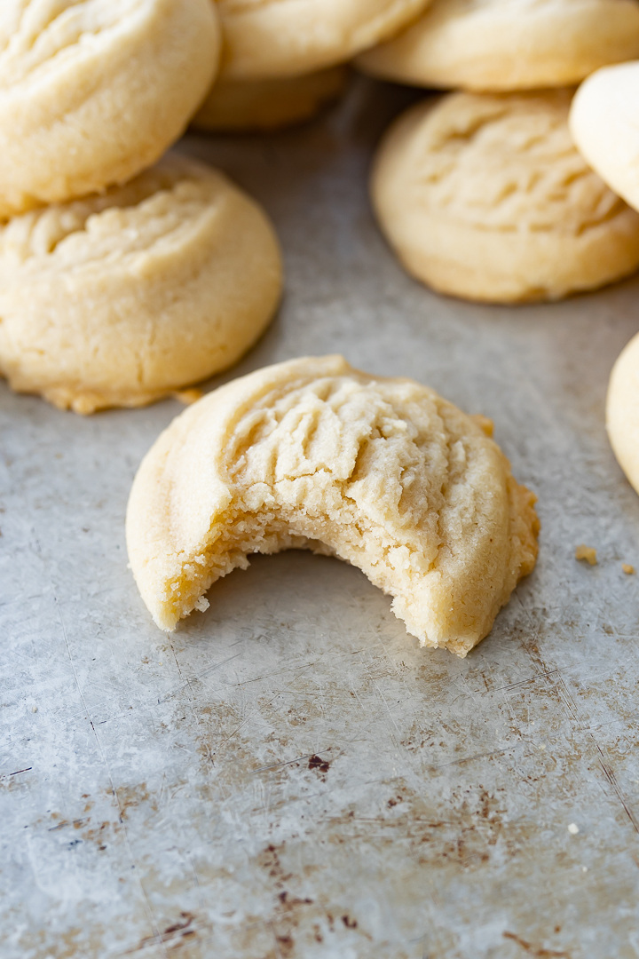brown butter sugar cookies on a cookie sheet, with a bite taken out of one.