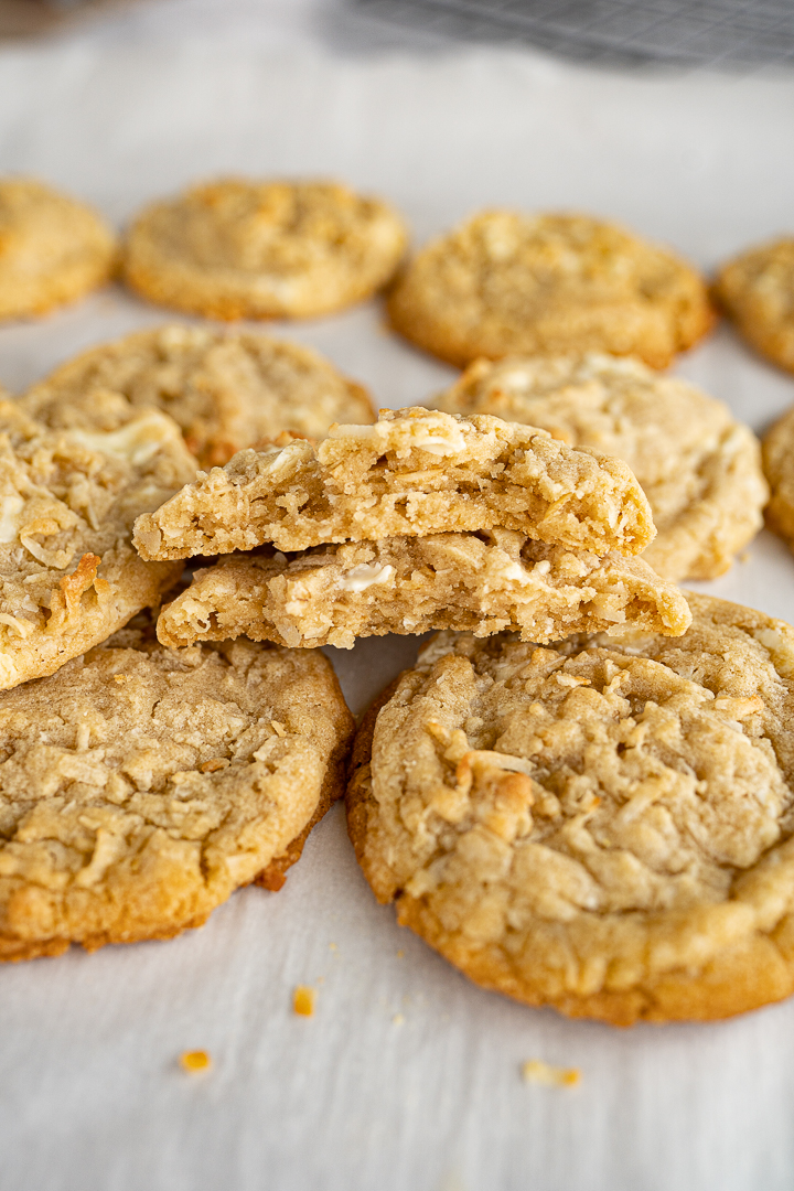 Two halves of a coconut cookie are stacked on each other on top of a tray of coconut cookies. 