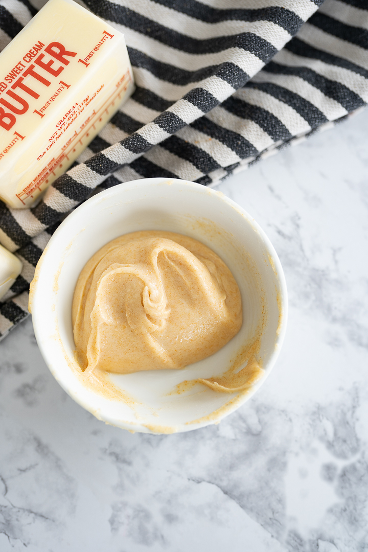 Chilled brown butter, back to solid form in a bowl on the counter with a black and white striped towel.