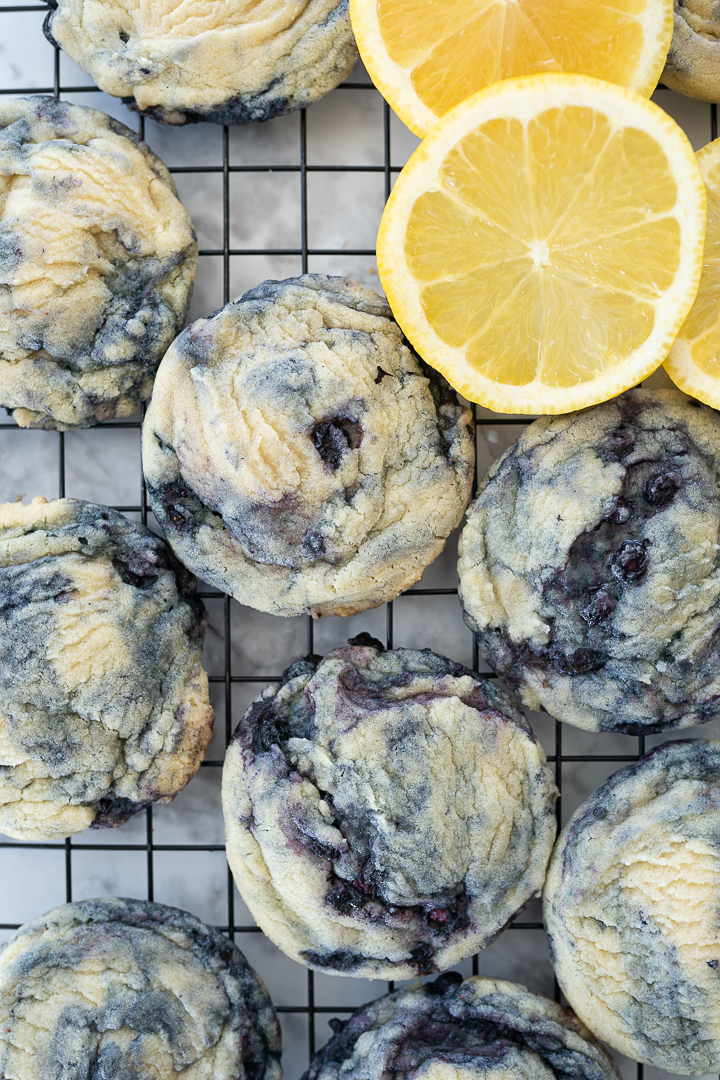 Arial view of blueberry lemon cookies on a cooling rack. Lemon slices adorn the upper right hand side of the cooling rack.