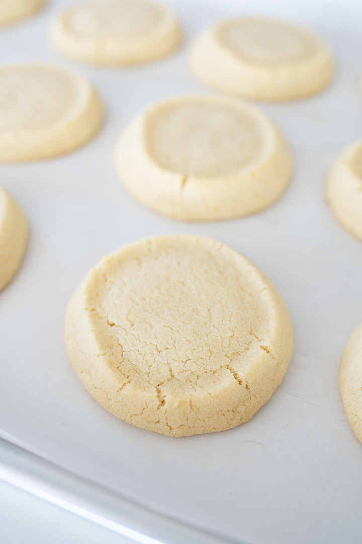 Close up of baked Pillsbury Sugar cookies sitting on a sheet pan lined with parchment paper. 