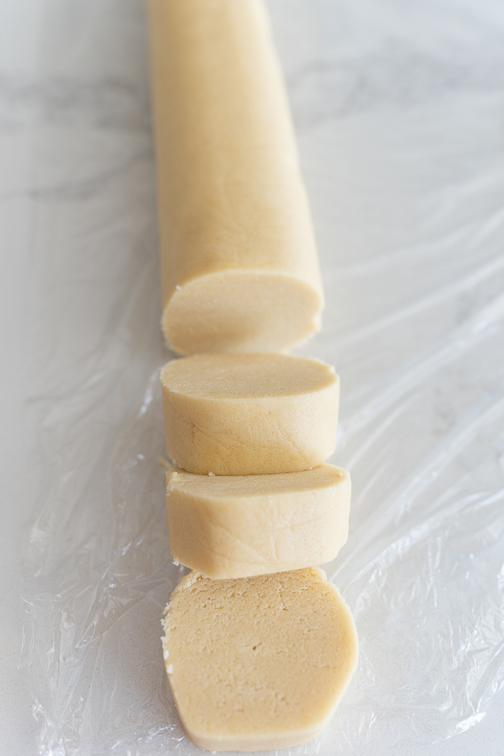 Roll of sugar cookie dough sliced, sitting on plastic wrap. 