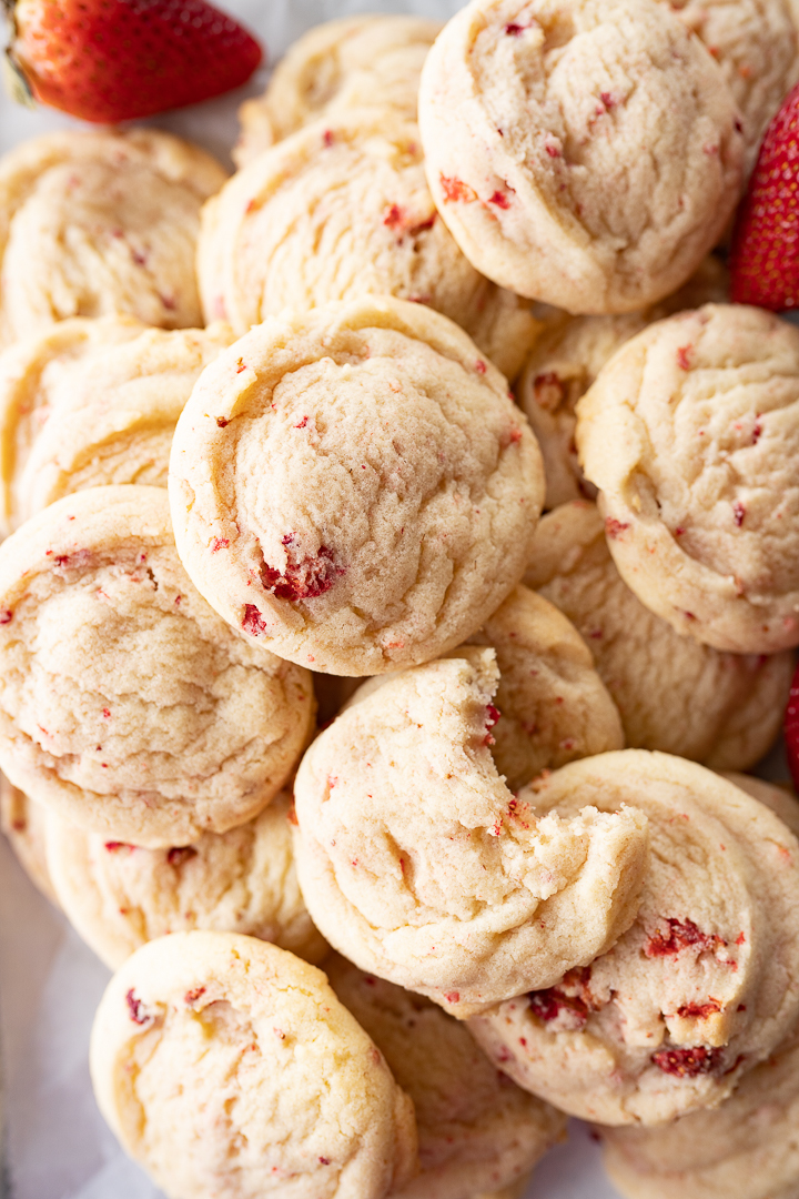 A close up of soft and chewy strawberry cookies piled high. The cookie on top has a bite taken out of it.