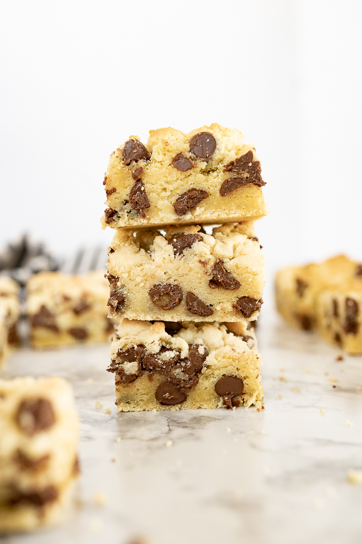 3 chocolate chip cake mix cookie bars are stacked on top of each other. In the background you can see additional bars that are blurred out.