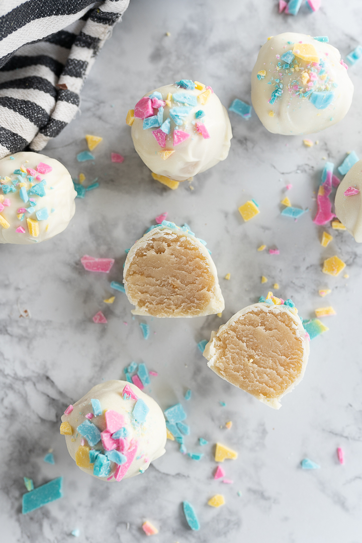 Cake balls scattered on a counter. One cake ball is sliced in half with the interior facing up. 